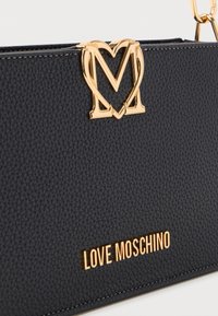 Μαύρη τσάντα χειρός από δερμάτινη υφή με χρυσό λογότυπο σε σχήμα καρδιάς "M" και επιγραφή "LOVE MOSCHINO" σε χρυστό μέταλλο.