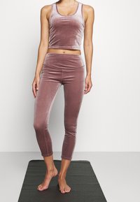 Top crop atletico in velluto e leggings in mauve attenuato. Design aderente con una morbida texture e una vita sagomata. La lunghezza termina a metà polpaccio.