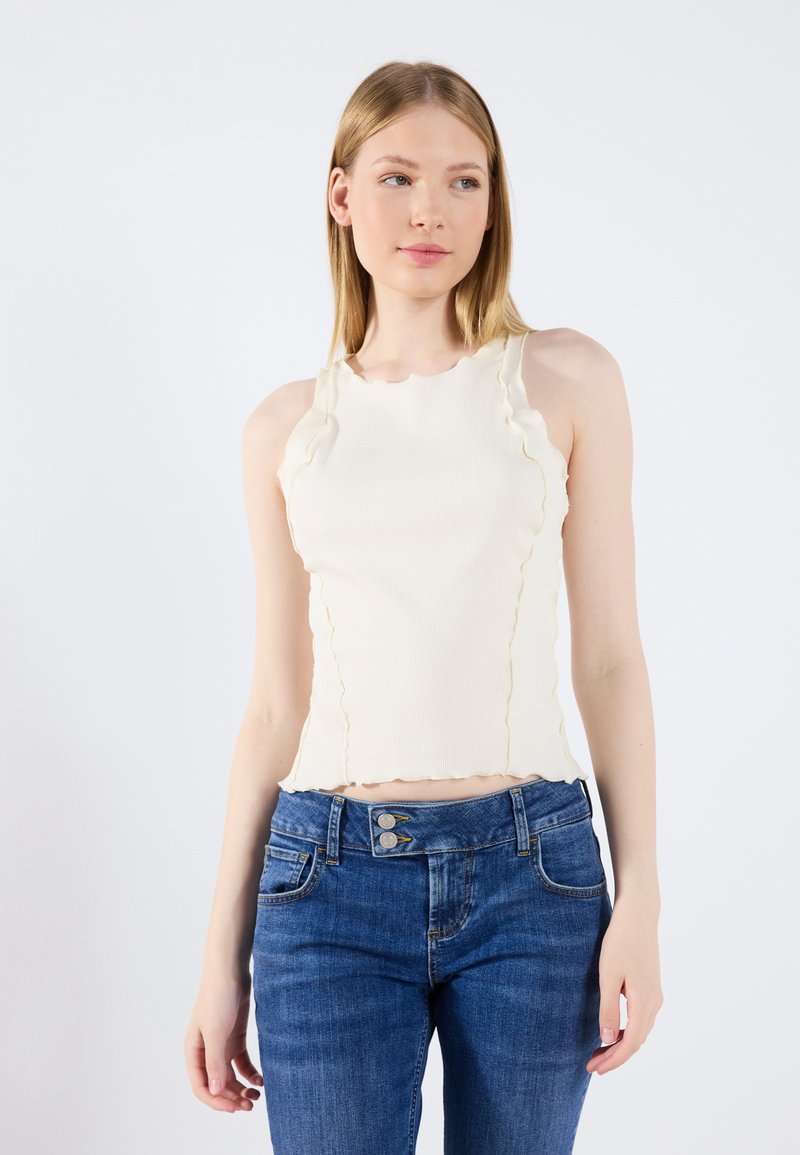 Kremfarget ribbestrikket tank topp med bølgede kanter, kombinert med mid-rise blå jeans med to-knapps lukking og klassiske lommer, ingen synlige mønstre.