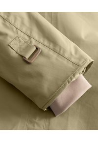 Manche de veste vert olive clair avec un poignet en rose doux replié. Comprend un D-ring en métal marron et un onglet cousu pour la fermeture. Texture lisse.