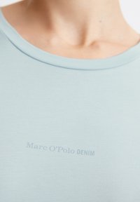 Vaaleansininen t-paita pehmeästä kankaasta, jossa pyöreä pääntie ja hillitty "Marc O'Polo DENIM" -logo painettuna lähellä kaulaa.