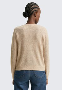 Suéter de punto beige con un corte relajado, escote redondeado y dobladillo acanalado, combinado con unos jeans de mezclilla azul. Textura suave, detalles mínimos.