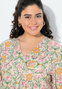 Blusa con stampa floreale caratterizzata da una scollatura a V, maniche corte e vivaci motivi rosa, giallo e verde su uno sfondo chiaro.