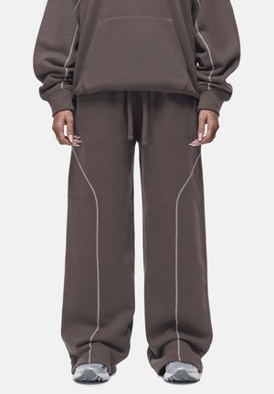 Bruine oversized hoodie en wijde broek set, gemaakt van zachte stof, met contrasterende witte stiksels langs de naden en een zak aan de voorkant.