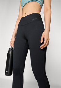 Leggings de sport noirs taille haute avec des coutures subtiles, accompagnés d'une bouteille d'eau noire. Le haut présente une couleur bleu clair.