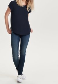 Námořnická blůza s krátkým rukávem spárovaná s tmavě modrými skinny džíny a bílými teniskami. Blůza má zaoblený lem a džíny mají vybledlý vzhled.