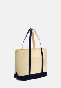 Borsa tote in tela beige con dettagli blu navy, forma rettangolare, doppie maniglie, e una tasca su un lato. Dettagli di cucitura robusta.