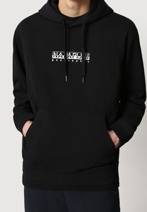 Person trägt einen schwarzen Hoodie mit Fronttaschen und weißem "Napapijri geographic" Logo in der Mitte der Brust.