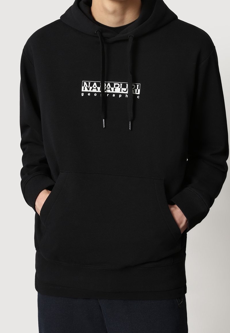 Personne portant un sweat à capuche noir avec des poches avant et un logo blanc "Napapijri geographic" centré sur la poitrine.