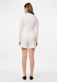 Haut long à manches longues beige clair à côtes avec un ourlet festonné, associé à un short assorti ; texture douce, silhouette ajustée, design simple.