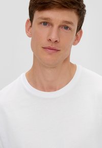 Weißes Rundhals-T-Shirt aus weicher Baumwolle. Glatte Textur mit minimaler Nahtführung und lockerer Passform, mit einem leicht gerippten Halsausschnitt.
