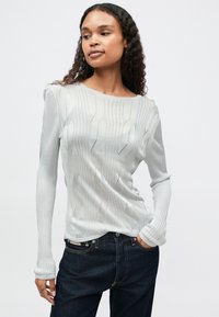 Ανοιχτό γκρι μακρυμάνικο πλεκτό μπλουζάκι με οριζόντιες ρίγες και λεπτομέρειες σε ανοιχτό πλέγμα. Μαλακή υφή, στρογγυλή λαιμόκοψη και εφαρμοστό σχέδιο.