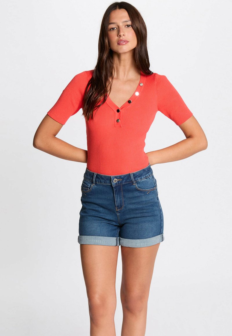 Geribbelde, koraalkleurige top met korte mouwen en een v-hals, versierd met drie zwarte knopen, gecombineerd met hoge, opgerolde denimshorts.