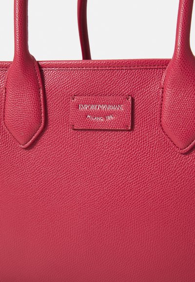 Geantă de mână roz din piele cu o textură granulată. Dispune de mânere duale și o plăcuță cu numele „Emporio Armani, Milano 1981.”