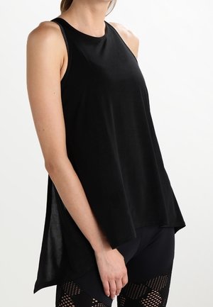 Kvinde iført en ærmeløs, løs sort top kombineret med sorte leggings med et netmønster på lårene.