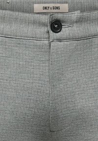Ceinture de pantalon grise texturée avec bouton noir et étiquette portant l'inscription "ONLY & SONS" cousue à l'intérieur de la ceinture arrière.