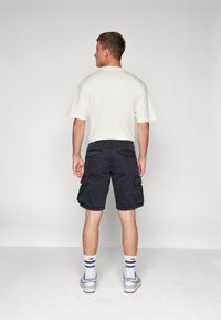 Black cargo shorts with side pockets, paired with a light-colored t-shirt. White socks with blue and red accents, and grey sneakers.
