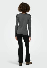 Grå langærmet top med pufskuldre, parret med sorte flared bukser og brune ankelstøvler. Glat stof og tætsiddende design.