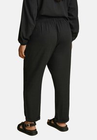 Svarta avslappnade byxor med elastisk midja, med en texturerad tyg och uppvikta fållar, parat med svarta sandaler.