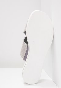 Chaussure grise à enfiler avec un dessus texturé et une semelle en caoutchouc blanc. Dispose d'un design superposé avec une bande élastique proéminente pour un maintien sécurisé.