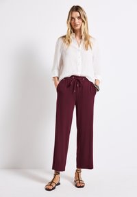 Burgundowe szerokie spodnie z elastycznym paskiem i sznurkiem. Połączone z białą koszulą z guzikami oraz czarnymi sandałami na paski.