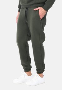 Pantaloni da tuta verde scuro realizzati in tessuto morbido, con polsini elastici e vita con coulisse, dotati di tasche laterali e una vestibilità rilassata.