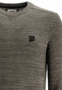 Grauer gestrickter Pullover mit einem strukturierten Muster, versehen mit einem schwarzen Logo-Patch und einem gerippten Rundhalsausschnitt.