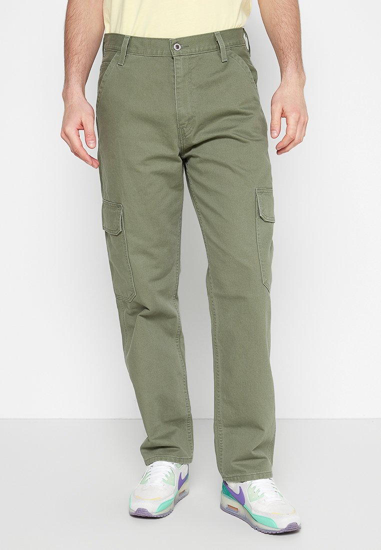 Pantalons cargo verts en coton avec une coupe droite, dotés de deux poches latérales et d'une fermeture à bouton à la taille. Portés avec des baskets blanches.