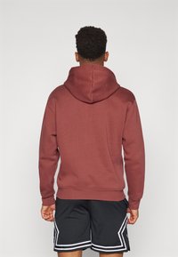 Felpa bordeaux con texture morbida e cappuccio, abbinata a pantaloni corti in rete neri con dettagli bianchi e un motivo a strisce laterali.
