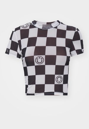 Crop top à motif damier noir et blanc, arborant des graphismes de smiley et de logo, avec des manches courtes et un col rond. Fabriqué en tissu extensible.