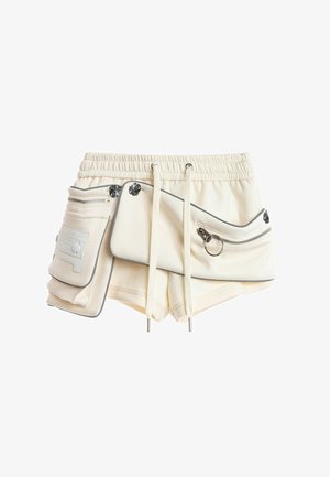 Pantalones cortos color crema con cintura elástica, cordón ajustable y dos grandes bolsillos con cremallera, adornados con detalles metálicos plateados.