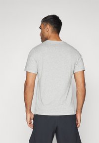 T-shirt grigio a girocollo, maniche corte, tessuto in morbido misto cotone, vestibilità rilassata, colore solido, orlo leggermente curvato, indossato con pantaloni corti scuri.