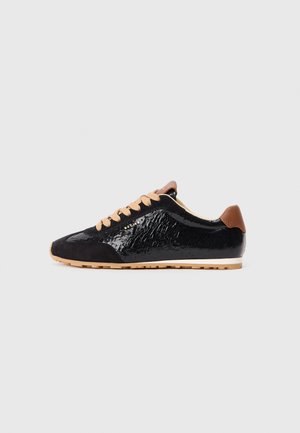 Schwarzer Sneaker aus Lackleder und Wildleder, mit einer strukturierten Oberfläche, beigen Schnürsenkeln und einem braunen Leder-Detail an der Ferse. Gummisohle.