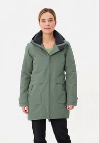 Groene waterdichte jas met een ritssluiting aan de voorkant, een zwarte kraag en twee grote zakken aan de voorkant. Voorzien van een capuchon en een ontwerp met een ontspannen pasvorm.