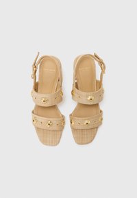 Beige woven sandals with two straps featuring gold floral embellishments and a gold buckle. Square toe design with a textured surface.