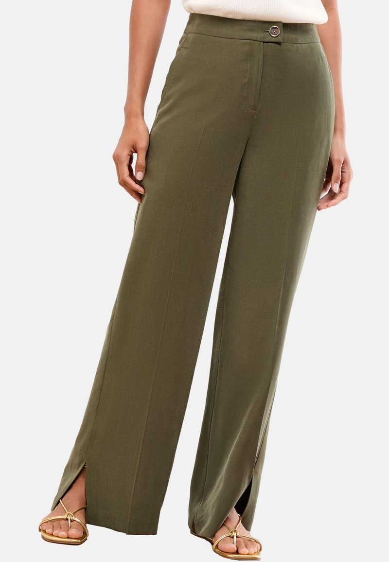 Femme portant un pantalon large vert olive avec des fentes à l'avant aux chevilles et des sandales beiges à brides.