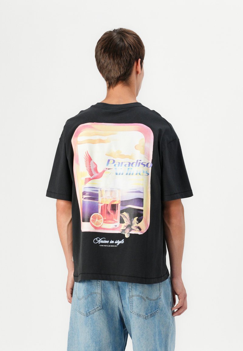 Zwarte katoenen T-shirt met een grote kleurrijke graphic van een vogel en een drankje op de achterkant, met de tekst "Paradiso Airlines" erboven.