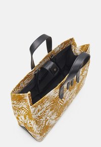 Sac cabas en toile avec un motif de feuilles tropicales jaunes et blanches ; doté de poignées en cuir noir et d'une poche intérieure sécurisée.