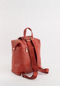 Mochila roja, estructurada, hecha de material liso. Cuenta con un cierre superior, dos asas y una correa desmontable con texto en relieve. Detalles de hardware dorado.