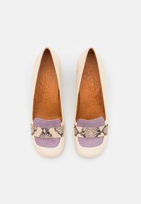 Une paire de mocassins crème avec des détails en forme de carré violet et une bande en cuir serpent à motifs sur chaque chaussure, vue de dessus.