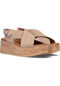 Sandales compensées en daim beige avec des lanières croisées, une semelle en liège et une boucle à la cheville. Semelle extérieure en caoutchouc antidérapante pour une meilleure traction.