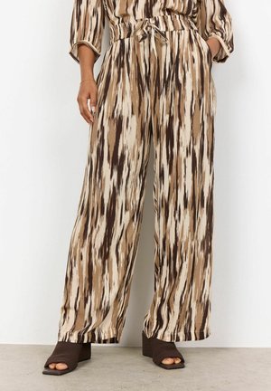 Woman wearing loose-fit, high-waist pants with brown, cream, and black vertical abstract pattern and open-toe brown heeled sandals.