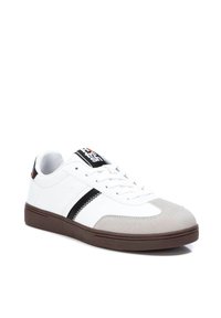Zapatilla blanca con puntera de ante gris, franja negra y suela de goma marrón. Presenta cordones y un logo en la lengüeta. Diseño clásico de corte bajo.