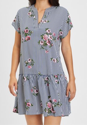 Kvinde iført kortærmet, knælængt marineblå og hvide lodrette stribede kjole med pink blomsterprint og en åben halsudskæring.