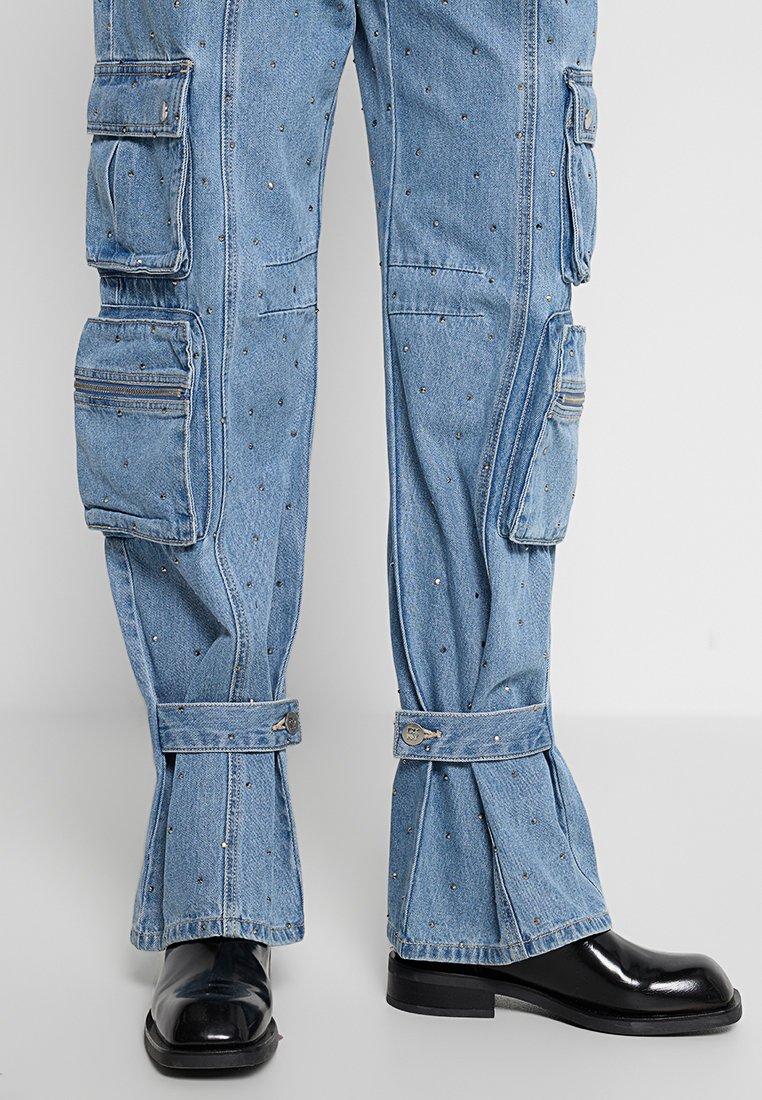 Blaue Denim-Cargohosen mit mehreren Taschen, dekorativen Nieten und umgeschlagenen Säumen. Sie zeichnen sich durch eine lockere Passform und detaillierte Nähte entlang der Nähte aus.