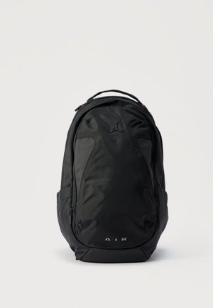 Mochila deportiva negra con asa superior, bolsillos laterales, compartimento frontal con cremallera y sutil logo Jumpman sobre el texto "AIR" en el panel frontal.