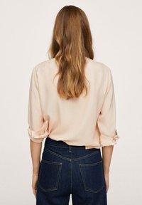 Helles rosa, geripptes Blusenshirt mit aufgerollten Ärmeln, kombiniert mit dunkelblauen Jeans mit Hintertaschen und kontrastierendem Nähen.