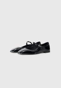 Black patent leather Mary Jane shoes feature a pointed toe, a strap with a buckle, and a flat sole with a textured finish.