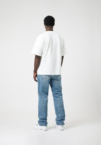 White cotton t-shirt with a relaxed fit, paired with light blue denim jeans. The shoes are white with green accents. Simple and functional design.