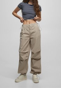 Pasiasty granatowy crop top, beżowe spodnie cargo z elastycznym pasem i sznurkiem, oraz jasne sneakersy. Gładki materiał, szeroki krój nogawek.